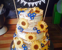 naked wedding cake decorated with sunflowers and blue daisies